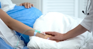 Primo piano del pancione di una donna in gravidanza, confortata da un'ostetrica per il rischio di affrontare un parto distocico